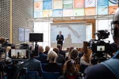 En mann holder en presentasjon foran et publikum. flere kamera i forgrunnen.