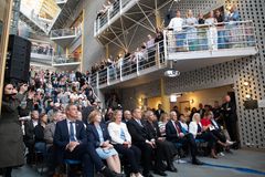 Et stort publikum samlet i en innendørs atrium, noen sitter, og andre står langs galleriene i etasjene over.