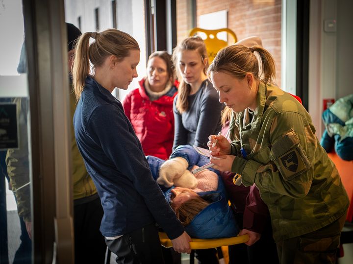 En gruppe mennesker deltar i en redningsøvelse, hvor en person ligger på en båre.