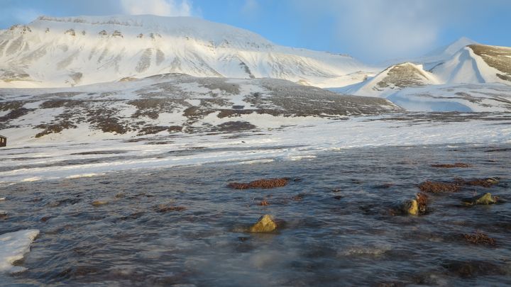Snødekte fjell med islagt terreng i forgrunnen under en delvis skyet himmel.