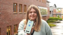 Ung dame står ut og holder fram en smartelefon med en nettside.