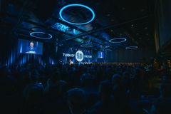 En person holder tale i en stor, fullsatt sal.