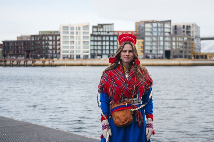dame med samisk kofte og fjord og bygninger i bakgrunnen
