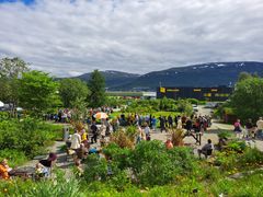 En travel dag i Botanisk hage i Tromsø med mange besøkende som går rundt blant grønne planter og fargerike blomster.