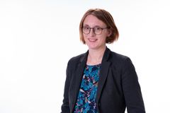 Profilbilde av kvinne med brunt hår og briller som smiler. Hvit bakgrunn.