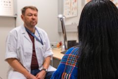 En helsearbeider sitter ved et skrivebord og snakker med en person som sitter i forgrunnen med ryggen til.