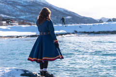 Kvinne i samisk kofte står ved en elv om vinteren.
