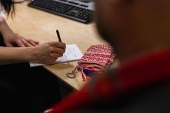 En person skriver notater ved et skrivebord med et samisk belte liggende ved siden av. En person sitter med ryggen til i forgrunnen.