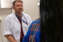 En person med ryggen til sitter foran en helsearbeider i hvit frakk.