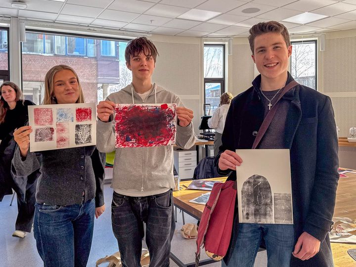 Tre elever holder opp fargerike kunst-trykk de har laget