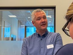 Mann med kort, grått hår og blå skjorte snakkermed journalist