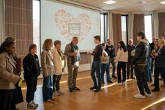 Mange folk er samlet på gulvet, snakker sammen og hilser