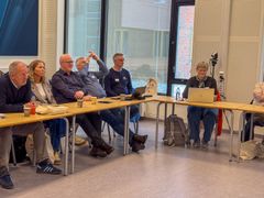 Menn og kvinner sitter i hestesko og samtaler/lytter