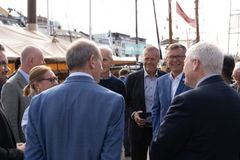 En gruppe mennesker snakker sammen på en kai, med båter i bakgrunnen.