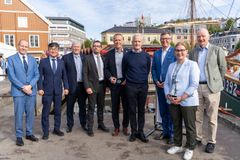En gruppe personer står samlet utendørs foran en båt og en bygning.