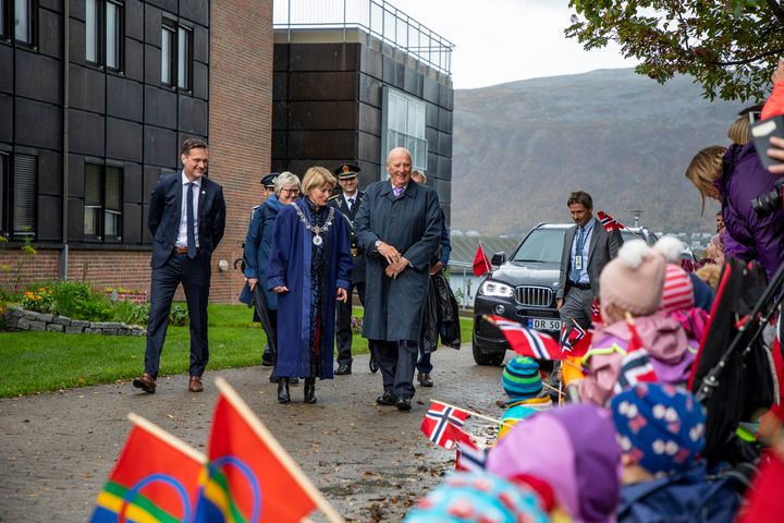 En%20gruppe%20mennesker%20g%E5r%20forbi%20barn%20som%20holder%20norske%20flagg.%20En%20bil%20og%20fjell%20er%20i%20bakgrunnen.