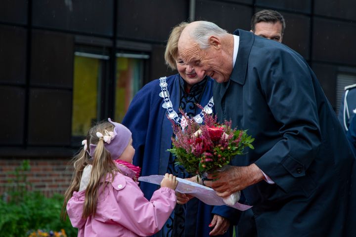 En eldre mann bøyer seg ned for å ta imot en blomsterbukett fra en liten jente i rosa jakke.