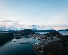 Kystsamfunn omgitt av fjord og snødekte fjell i Nord-Norge, sett fra luften.