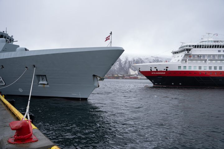 Grått marinefartøy og Hurtigruteskipet Otto Sverdrup ligger ved kai i Tromsø, med snødekte fjell i bakgrunnen.