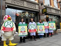 Dyrevenner utkledd som matkontrollører i hvite laboratoriefrakker som holder protestskilt mot McDonald’s salg av turbokylling.