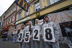 Frivillige kledd i heldekkende klær står foran en McDonald's og holder tallene 3528.