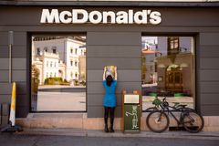 Kvinne i blå kjole henger opp en plakat på veggen utenfor en McDonald's restaurant.