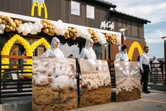 Fire personer i beskyttelsesdrakter holder bilder av kyllinger foran en McDonald's restaurant pyntet med ballonger.
