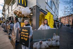 Aktivister i smitteverndrakter står på rad utenfor en McDonald's-restaurant og holder plakater med bilder av kyllinger og tekst om trange dyreforhold, som en protest mot kyllingproduksjon.