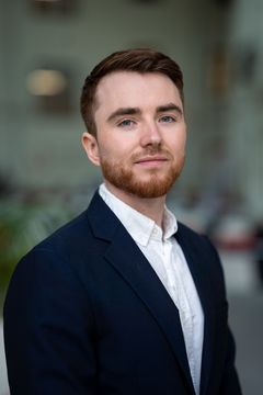 Portrettfoto av Niklas Fjeldberg, en mann med rødt skjegg iført mørk blazer og hvit skjorte, fotografert utendørs mot en uklar bakgrunn.