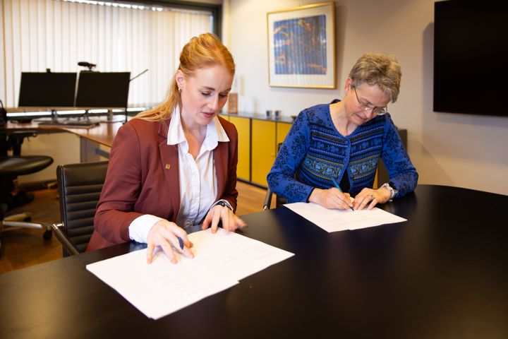 To kvinner ved bord signerer på hvite ark