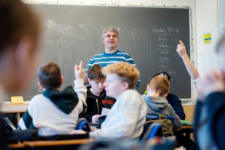 Mann står foran en tavle. En gruppe ungdommer sitter ved pulter.