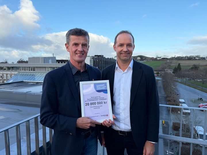 To menn i dress holder eit diplom mellom seg.