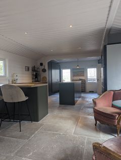 Åpen planløsning på en hytte, med en kjøkkenøy og en elegant stueplass med vintage lenestoler.