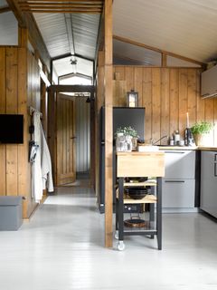 Interiør av et moderne kjøkken med trepaneler og et gråmalt tregulv.
