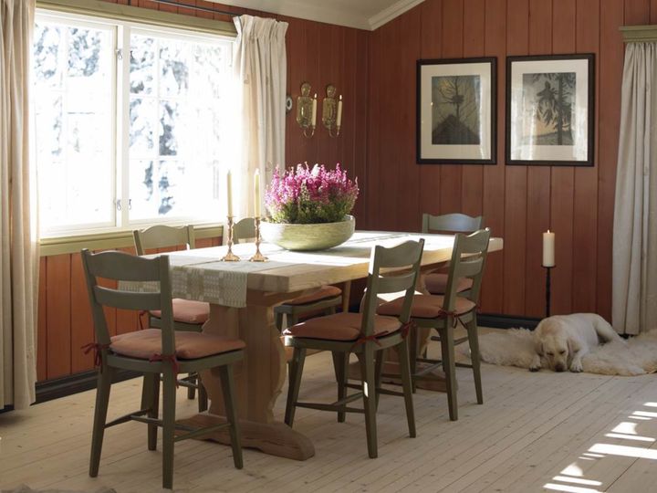 Alternativ tekst: Et koselig spisestueinteriør på hytta, med et langt bord, stoler, et vindu og en hvilende hund på gulvet.