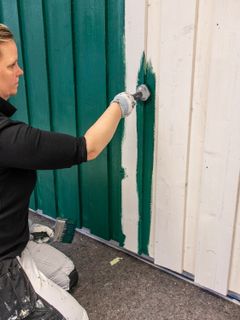 Person maler en hvit vegg med grønn maling.