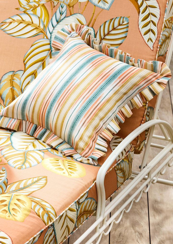 Pute med stripete mønster på en stol med blad-mønster i lignende farger.