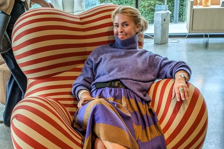 Charlotte%20Holberg%20Sveinsen%20sitter%20i%20en%20stor%20r%F8d-%20og%20hvitstripet%20lenestol.