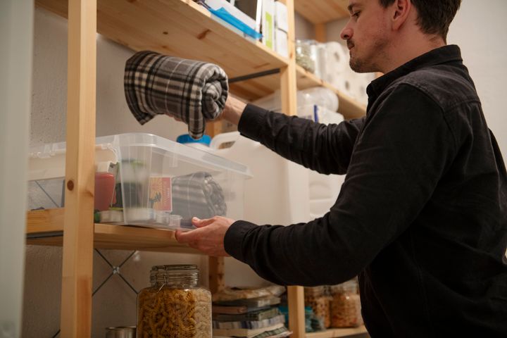 Mann%20rydder%20i%20et%20matskap%20og%20legger%20et%20rutete%20t%F8ystykke%20i%20en%20plastkasse.