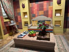 Stilfull stue med mønstret sofa, rutete vegger og stort puffbord med blomster og grønne epler.