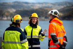 Tre personer i verneutstyr har en diskusjon utendørs nær et vann på fjellet.