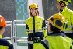 En gruppe personer i verneutstyr, inkludert gule hjelmer og jakker, står sammen inne i et kraftverk.