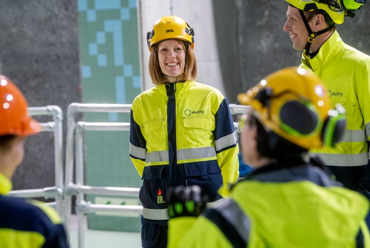 En gruppe personer i verneutstyr, inkludert gule hjelmer og jakker, står sammen inne i et kraftverk.