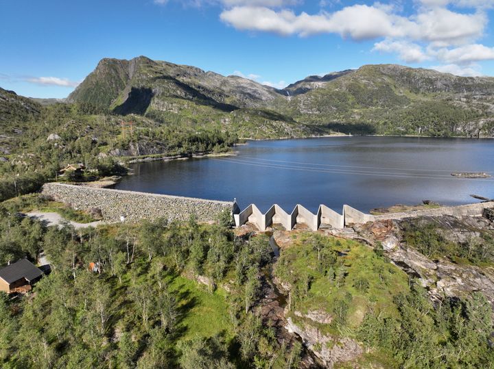 Bilde av Kvitingsvatnet omgitt av fjell og skoger, med en damkonstruksjon i forgrunnen.