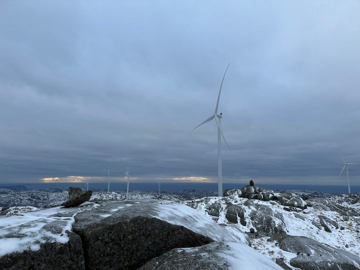 En vindpark med flere turbiner på en snødekt åsside under overskyet himmel.