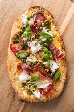 En luftig pinsabunn toppet med coppaskinke, mozzarella, pesto, basilikum og pinjekjerner.