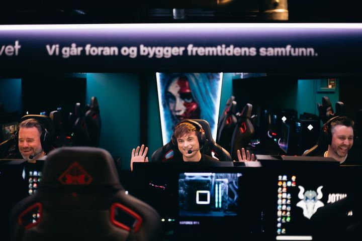 Tre menn som sitter på rekke og gamer, alle smiler og ler