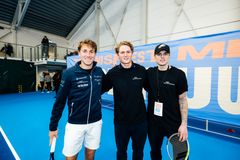 Tennisspillere Casper Ruud og Simen Sunde Bratholm står i en tennishall sammen med Gustav Magnar Witzøe og smiler mot kameraet