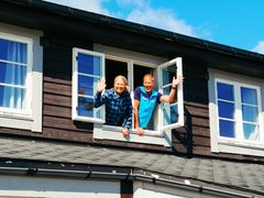 To personer står i et vindu på Finsehytta og smiler mens de vinker.
