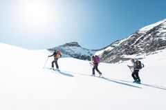 Tre personer går oppover en bakke med ski.